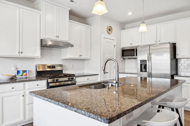 kitchen featuring hanging light fixtures, white cabinetry, stainless steel appliances, and a kitchen island with sink