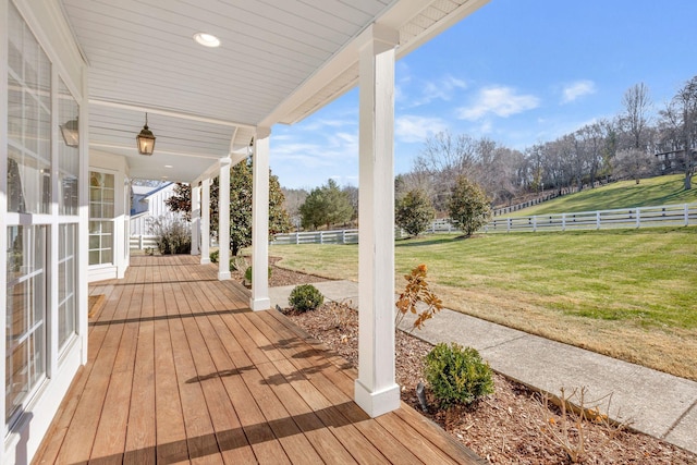 wooden terrace featuring a lawn, a rural view, and a porch