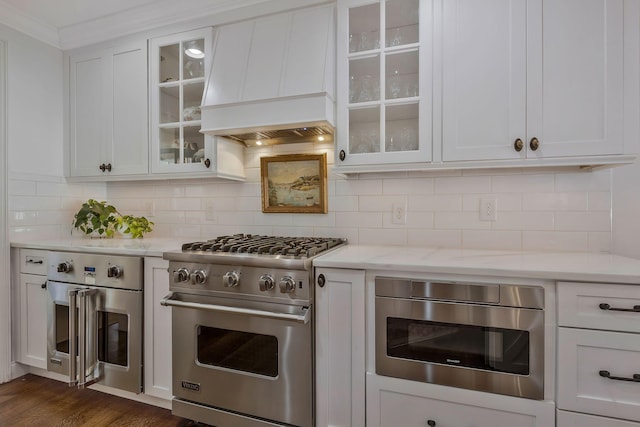 kitchen with custom exhaust hood, dark wood-type flooring, light stone countertops, white cabinetry, and stainless steel appliances