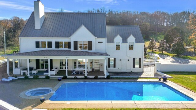 rear view of house featuring a swimming pool with hot tub and a patio