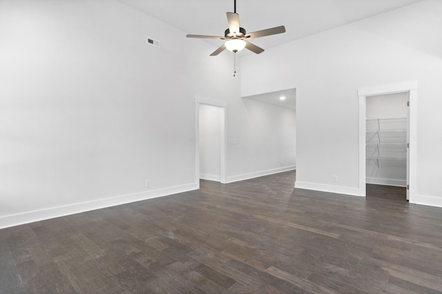 unfurnished living room featuring ceiling fan, dark wood-type flooring, and a high ceiling