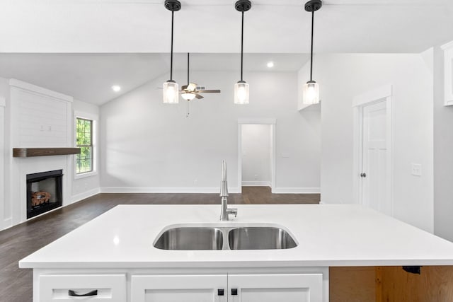 kitchen featuring lofted ceiling, dark wood-type flooring, a center island with sink, sink, and hanging light fixtures