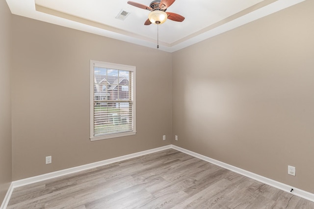 empty room featuring a tray ceiling, ceiling fan, and light hardwood / wood-style flooring