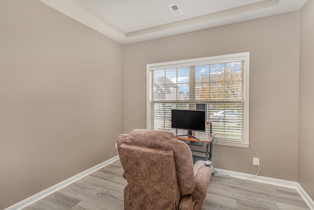 office space featuring a tray ceiling and light hardwood / wood-style flooring