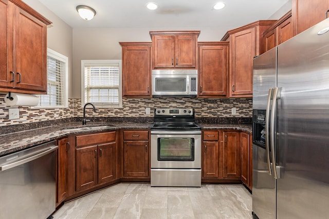 kitchen with backsplash, stainless steel appliances, dark stone countertops, and sink