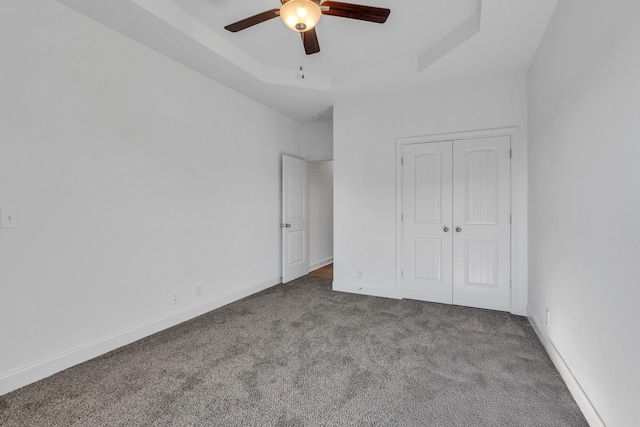 unfurnished bedroom with baseboards, a raised ceiling, a ceiling fan, carpet, and a closet