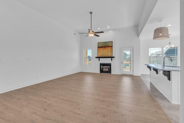 unfurnished living room with a large fireplace, ceiling fan with notable chandelier, a sink, and light wood-style floors