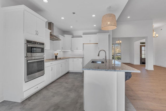 kitchen featuring white cabinetry, a sink, wall chimney range hood, and an island with sink