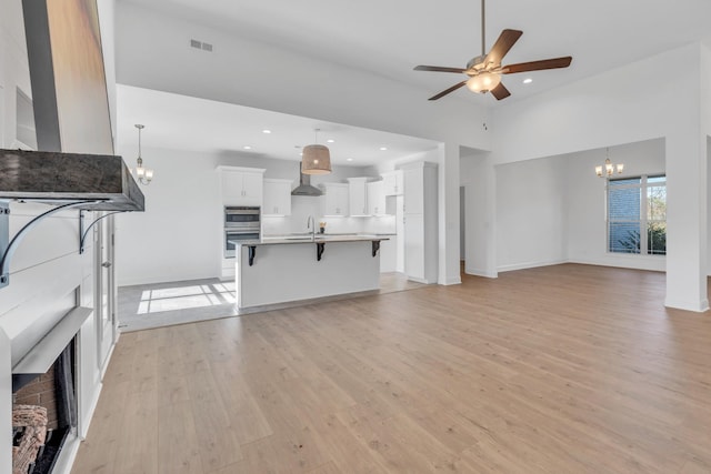 unfurnished living room featuring recessed lighting, ceiling fan with notable chandelier, a sink, visible vents, and light wood-type flooring