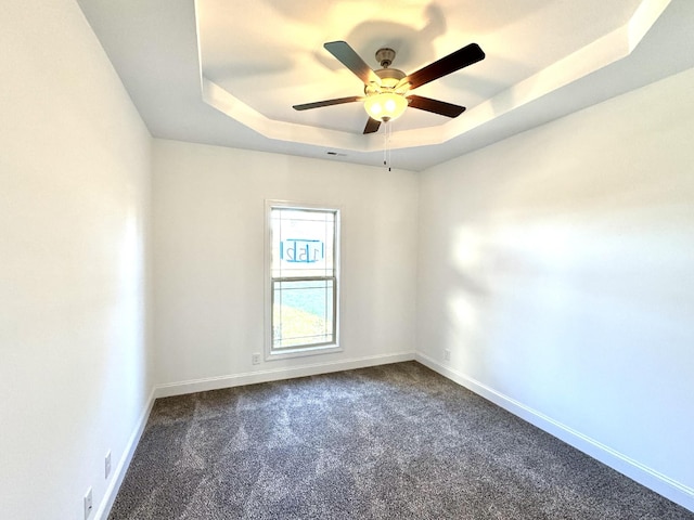 unfurnished room featuring a ceiling fan, dark colored carpet, a raised ceiling, and baseboards