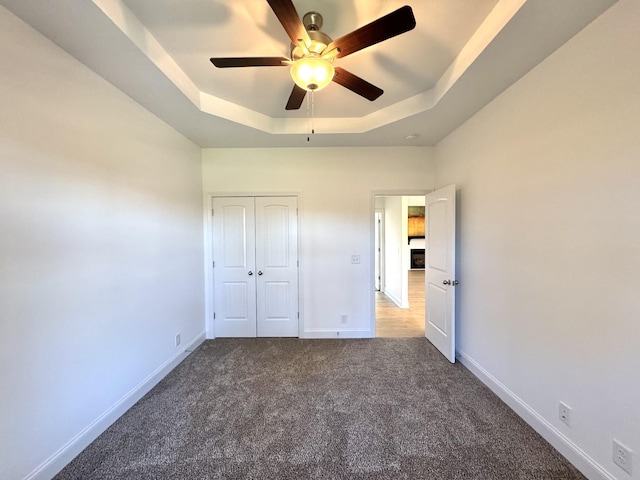 unfurnished bedroom with carpet floors, a tray ceiling, a closet, and baseboards