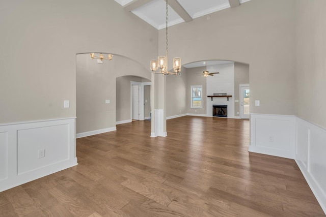 unfurnished living room with beamed ceiling, hardwood / wood-style floors, crown molding, a high ceiling, and ceiling fan with notable chandelier