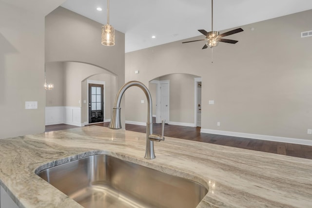 kitchen featuring pendant lighting, ceiling fan, sink, a high ceiling, and light stone countertops