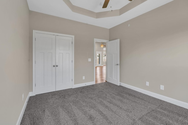 unfurnished bedroom with ceiling fan, a tray ceiling, a closet, and carpet flooring