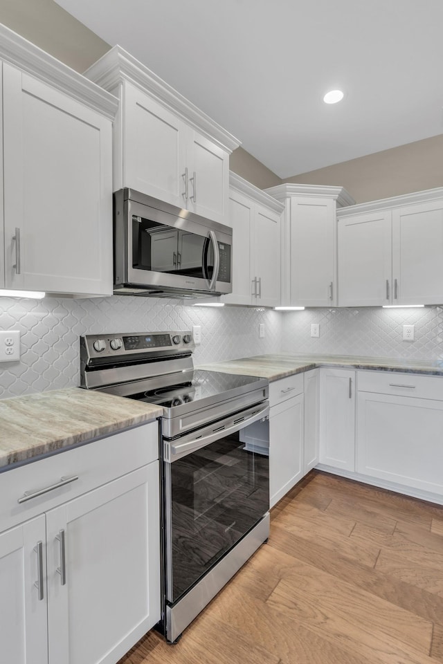 kitchen with decorative backsplash, white cabinetry, appliances with stainless steel finishes, and light hardwood / wood-style flooring