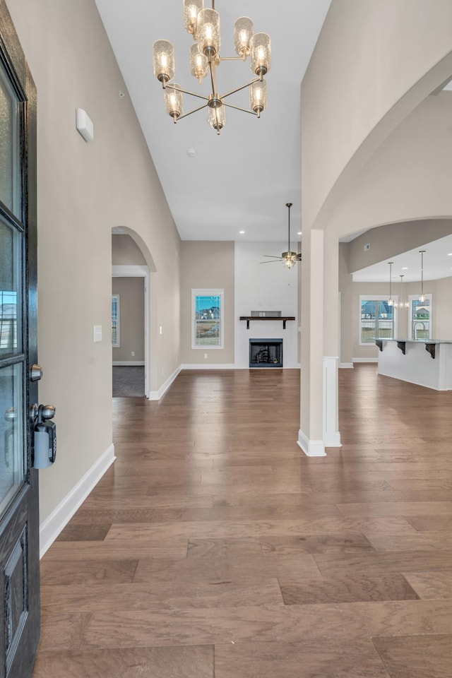 unfurnished living room with hardwood / wood-style flooring, ceiling fan with notable chandelier, and a high ceiling