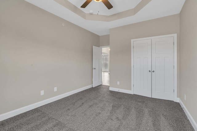 unfurnished bedroom featuring ceiling fan, a closet, carpet floors, and a raised ceiling