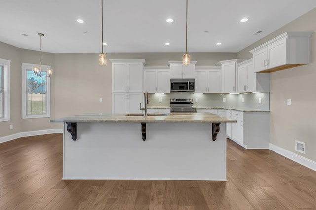 kitchen with sink, stainless steel appliances, a center island with sink, and decorative light fixtures