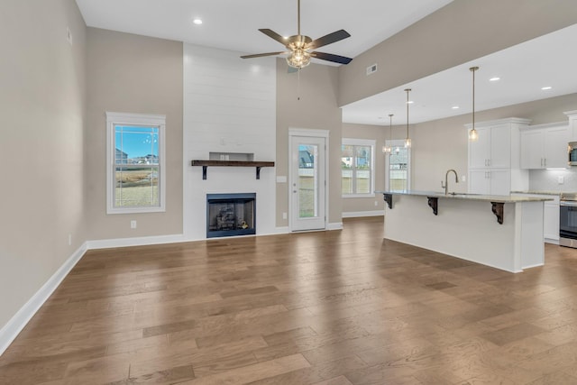 unfurnished living room featuring a fireplace, hardwood / wood-style flooring, a high ceiling, and ceiling fan