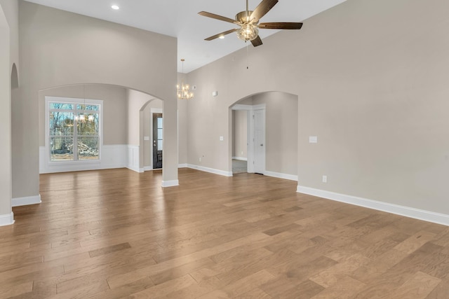 unfurnished living room with ceiling fan with notable chandelier, light hardwood / wood-style floors, and high vaulted ceiling