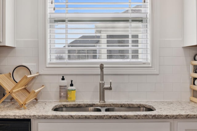 interior details featuring decorative backsplash, light stone counters, white cabinetry, and sink