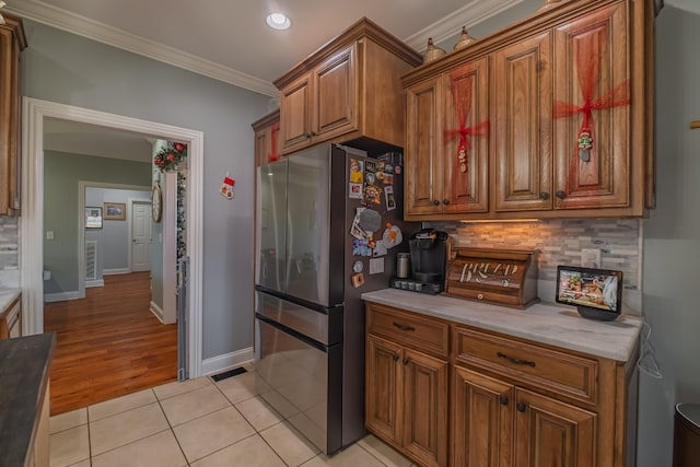 kitchen featuring light hardwood / wood-style flooring, decorative backsplash, dark stone countertops, ornamental molding, and stainless steel refrigerator