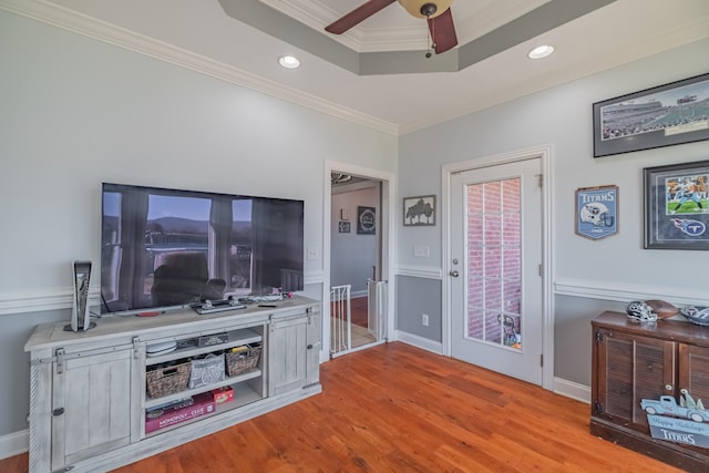 living room featuring a tray ceiling, recessed lighting, light wood-type flooring, and ornamental molding