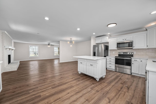 kitchen featuring appliances with stainless steel finishes, tasteful backsplash, white cabinetry, a center island, and a brick fireplace