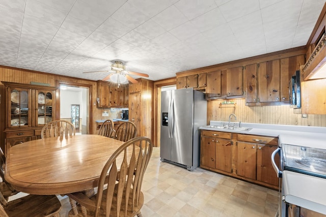 kitchen featuring appliances with stainless steel finishes, sink, ceiling fan, and wood walls