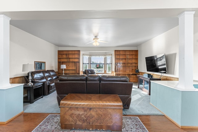 living room with decorative columns, wood-type flooring, wooden walls, and ceiling fan