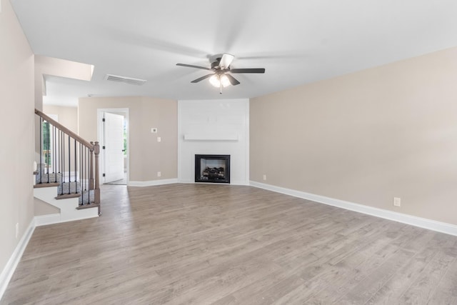 unfurnished living room featuring a fireplace, a ceiling fan, light wood-type flooring, baseboards, and stairs