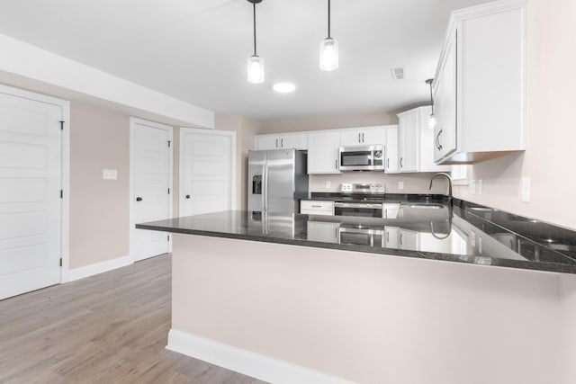 kitchen featuring a peninsula, appliances with stainless steel finishes, dark stone countertops, and a sink