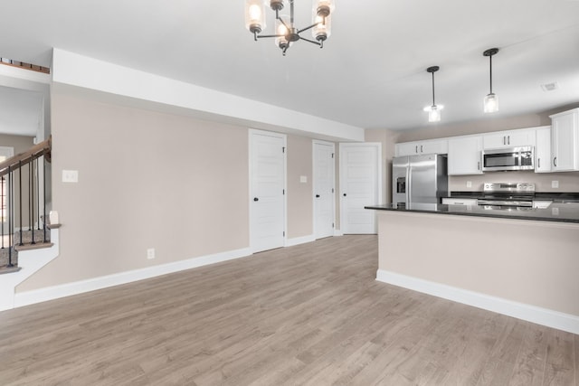 kitchen with light wood finished floors, white cabinets, dark countertops, decorative light fixtures, and stainless steel appliances