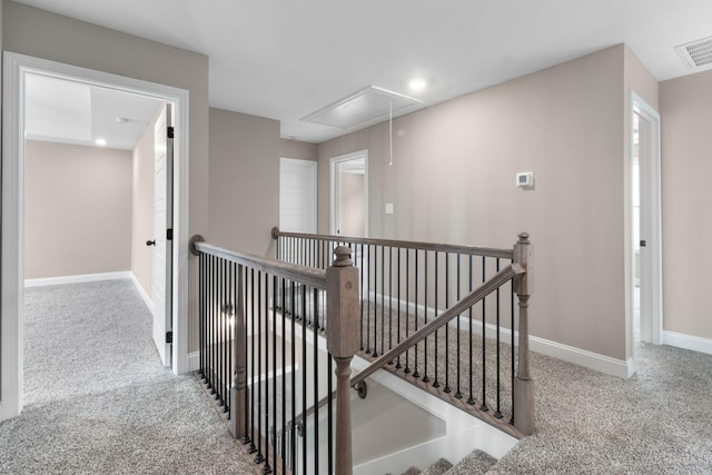 hallway featuring carpet flooring, visible vents, an upstairs landing, baseboards, and attic access