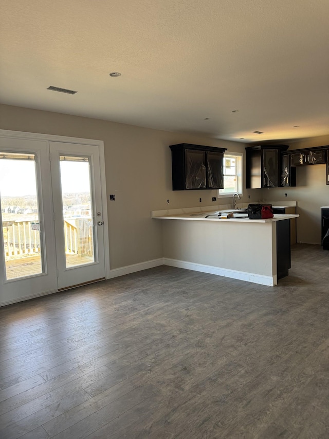 kitchen with dark wood-style floors, visible vents, a sink, a peninsula, and baseboards