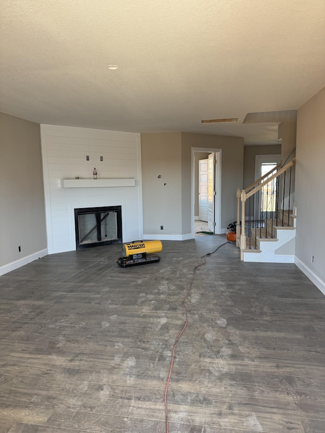 unfurnished living room featuring a fireplace, a textured ceiling, wood finished floors, baseboards, and stairs