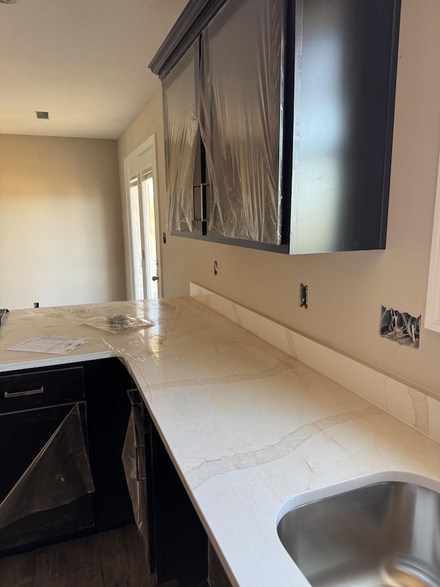 kitchen with dark cabinetry, a sink, visible vents, and light stone countertops