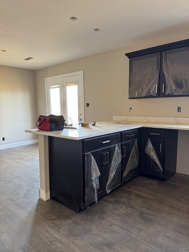 kitchen with dark cabinets, dark wood-type flooring, a peninsula, and baseboards