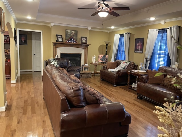 living room with light wood-type flooring, a raised ceiling, ceiling fan, and ornamental molding