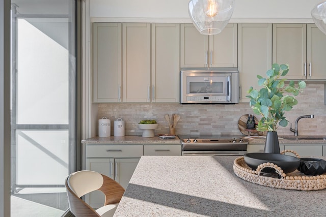 kitchen featuring decorative backsplash, stainless steel appliances, light stone counters, and sink