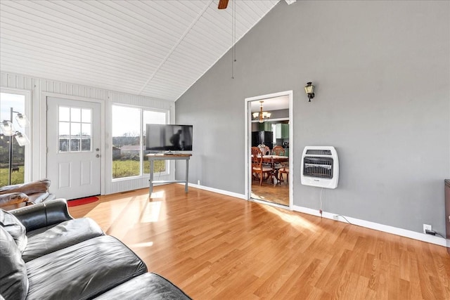 unfurnished living room with ceiling fan with notable chandelier, light wood-type flooring, high vaulted ceiling, and heating unit