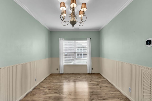 empty room with hardwood / wood-style floors, ornamental molding, and an inviting chandelier