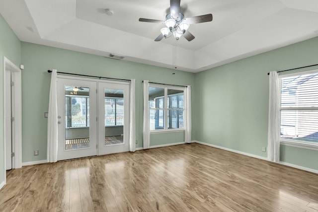 empty room with a tray ceiling, ceiling fan, light hardwood / wood-style flooring, and french doors