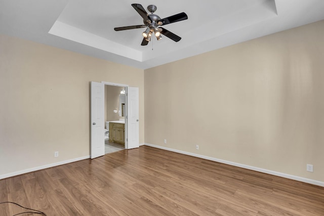 spare room featuring a tray ceiling, ceiling fan, and light hardwood / wood-style flooring