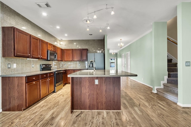 kitchen featuring an inviting chandelier, an island with sink, light hardwood / wood-style floors, appliances with stainless steel finishes, and ornamental molding