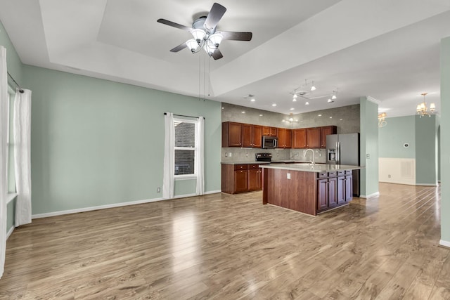 kitchen with ceiling fan with notable chandelier, light hardwood / wood-style floors, a kitchen island with sink, and appliances with stainless steel finishes