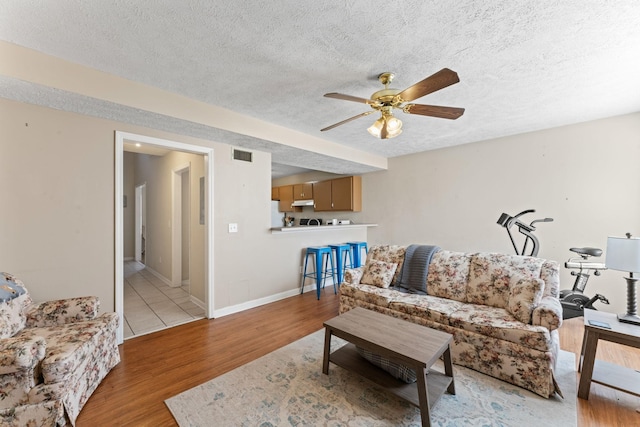 living room featuring a textured ceiling, light hardwood / wood-style floors, and ceiling fan