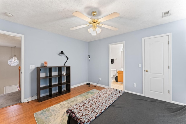 bedroom with ceiling fan, light hardwood / wood-style floors, a textured ceiling, and connected bathroom