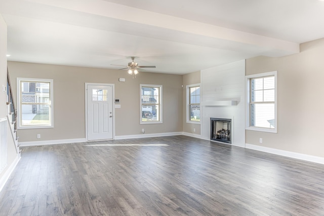 unfurnished living room with dark wood-style floors, a fireplace, baseboards, and a wealth of natural light