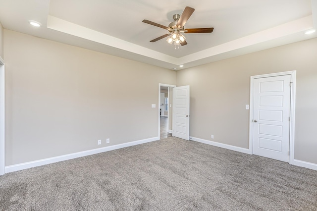 carpeted spare room featuring recessed lighting, a tray ceiling, baseboards, and ceiling fan